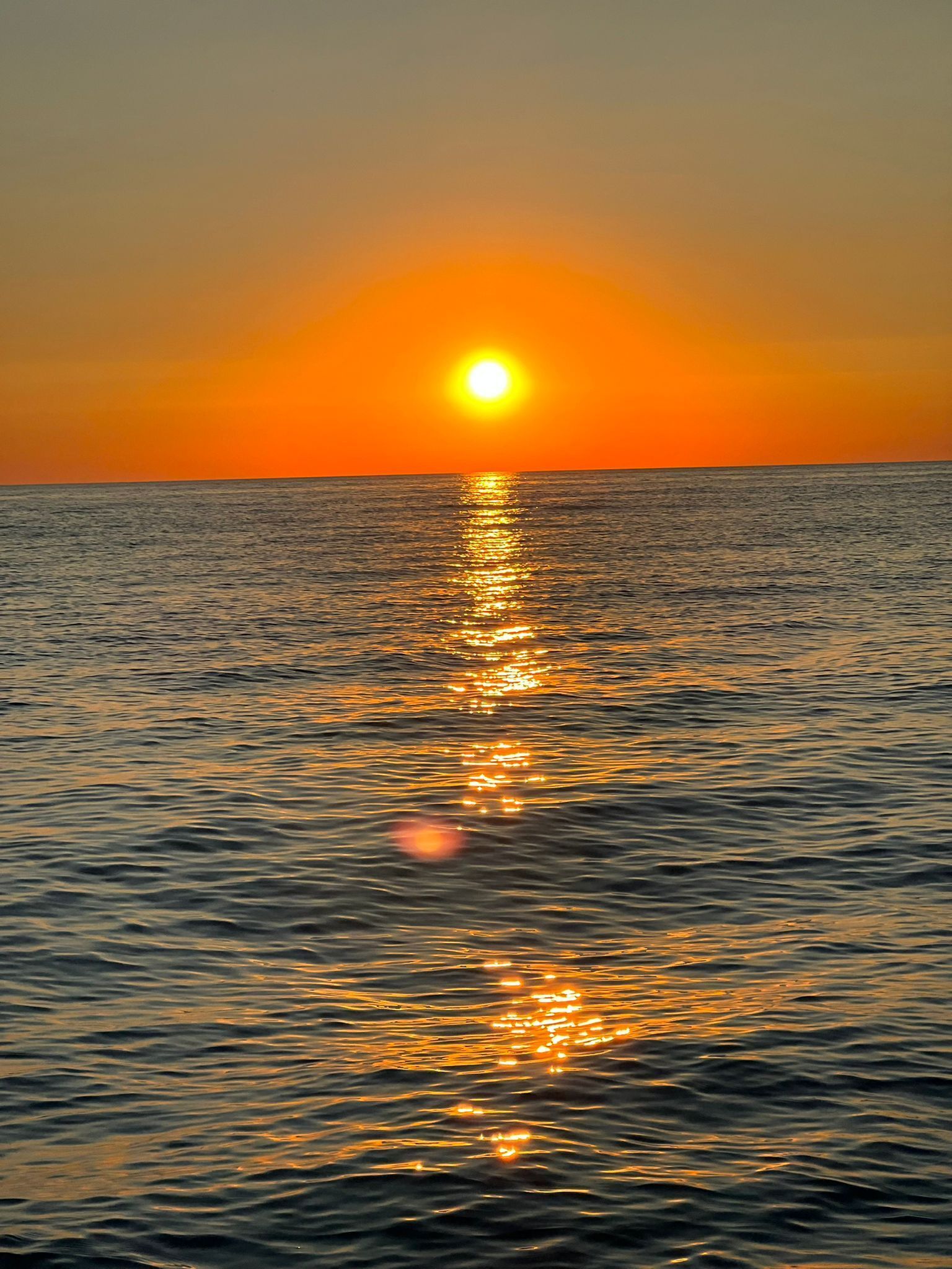 A sunset over a calm sea with the sun reflecting on the water.