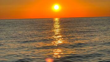 A sunset over a calm sea with the sun reflecting on the water.