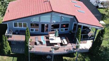 A large house with a red roof, multiple windows, and a deck with outdoor furniture.