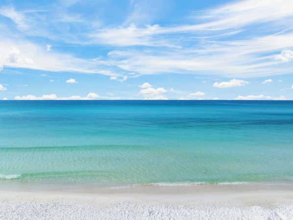 A beach with clear turquoise water and a sandy shore under a blue sky with scattered clouds.