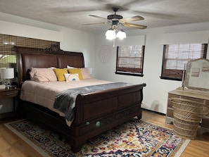 Classic bedroom with a large bed, nightstand, and lamp, featuring artwork and a cozy area rug.