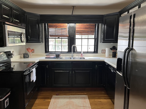Features a kitchen with dark cabinetry, stainless steel appliances, a large window, and a sink, oven, and refrigerator.
