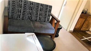 A compact living space with a sofa, a small table, a trash bin, and a wooden cabinet. - Modern studio decorated in African colors at the rear of a spacious villa. (Yaoundé)
