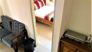 A room with a bed, a small table with a basket, and a cabinet. - Modern studio decorated in African colors at the rear of a spacious villa. (Yaoundé)