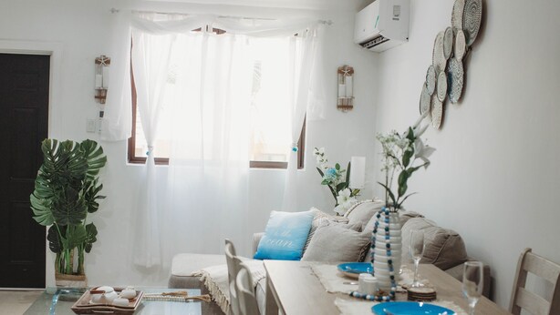 Un área de comedor con una mesa de vidrio, sofá color beige y una planta grande.