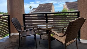 Un área de estar al aire libre techada con sillas de mimbre y una pequeña mesa redonda, con vista a un barrio residencial.