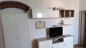 A room with a white wardrobe, a television on a white cabinet, and a brick archway.