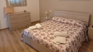 A bedroom with a bed, a dresser, a nightstand, a lamp, and a floral painting on the wall.