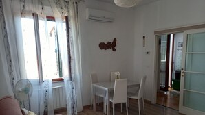 A living room with a sofa, a dining table with chairs, a decorative wall piece, and a sliding glass door leading to another room.