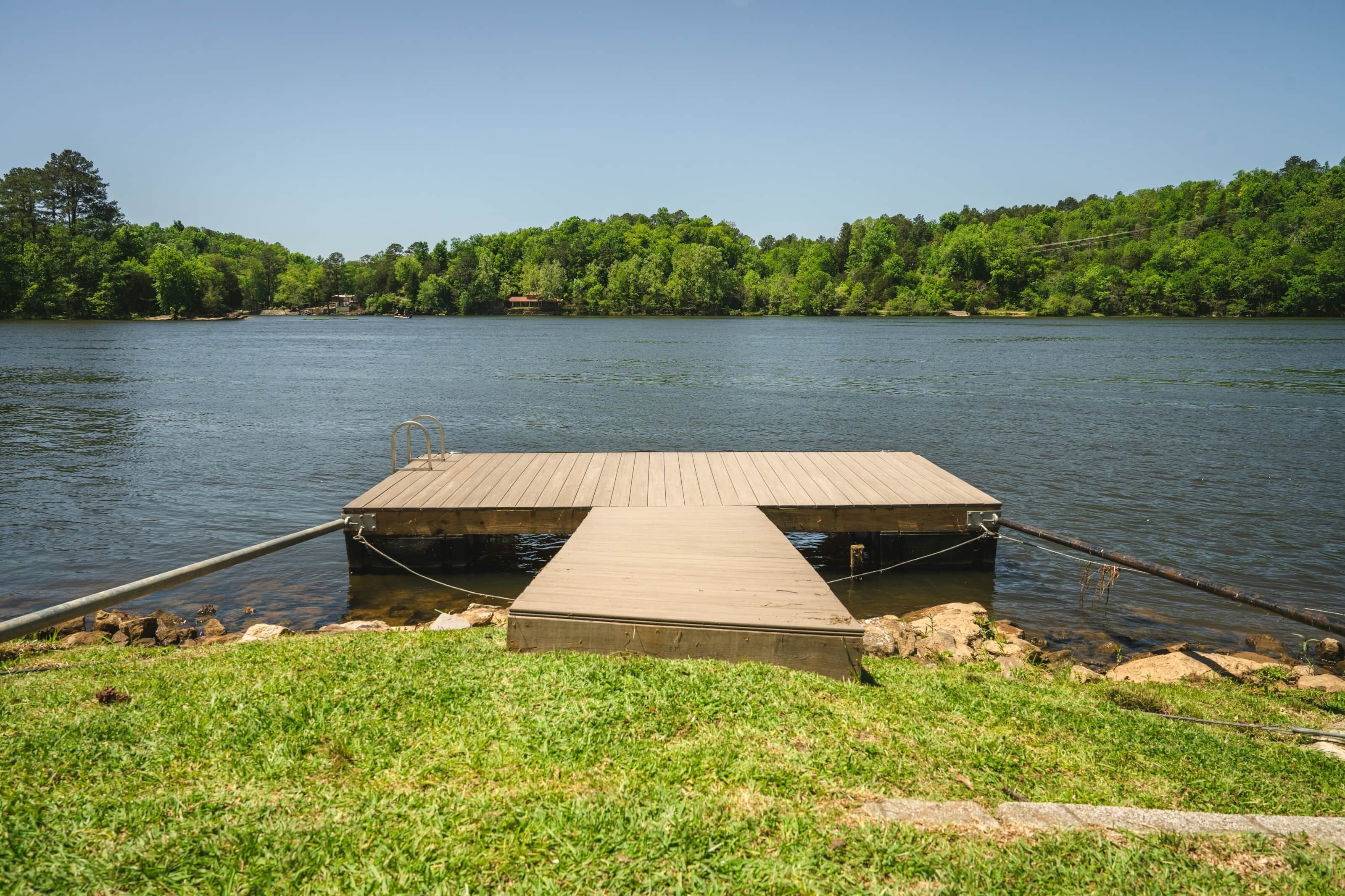A wooden dock extending into a calm lake, surrounded by lush greenery and a clear sky.