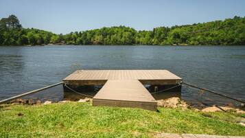 A wooden dock extending into a calm lake, surrounded by lush greenery and a clear sky.