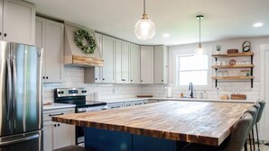 A modern kitchen with white cabinets, a wooden island, stainless steel appliances, and pendant lighting.