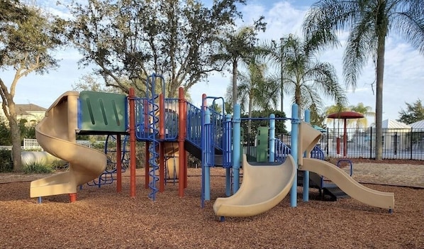 Explore the playground's spiral slide and multi-level climbing frame, surrounded by a secure fence and lush greenery.