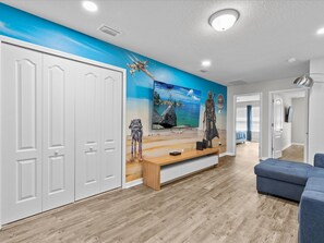 Relax in this stylish living room with a large flat-screen TV, comfortable sofa, and a unique blue accent wall featuring a vibrant mural.