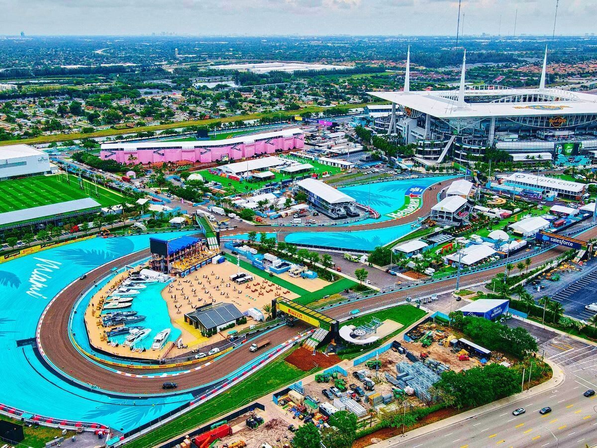 A large stadium with a central track, surrounded by various buildings and a parking area.