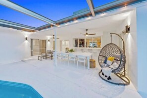 Un espacio exterior moderno con piscina, mobiliario blanco y una silla colgante.