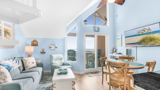 A spacious living area with a sofa, a coffee table, and a dining table with chairs. There is a large window offering a view of the beach. - Top Floor with Amazing views of the Gulf - steps from the State Park Trails (Gulf Shores)