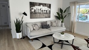 A modern living room with a light grey sofa, a round coffee table, and a large California-themed artwork on the wall. - Pet & Kid-Friendly Beach Retreat Near Town  +EVC , Fire Pit , Beach & Baby Gear! (Santa Barbara)