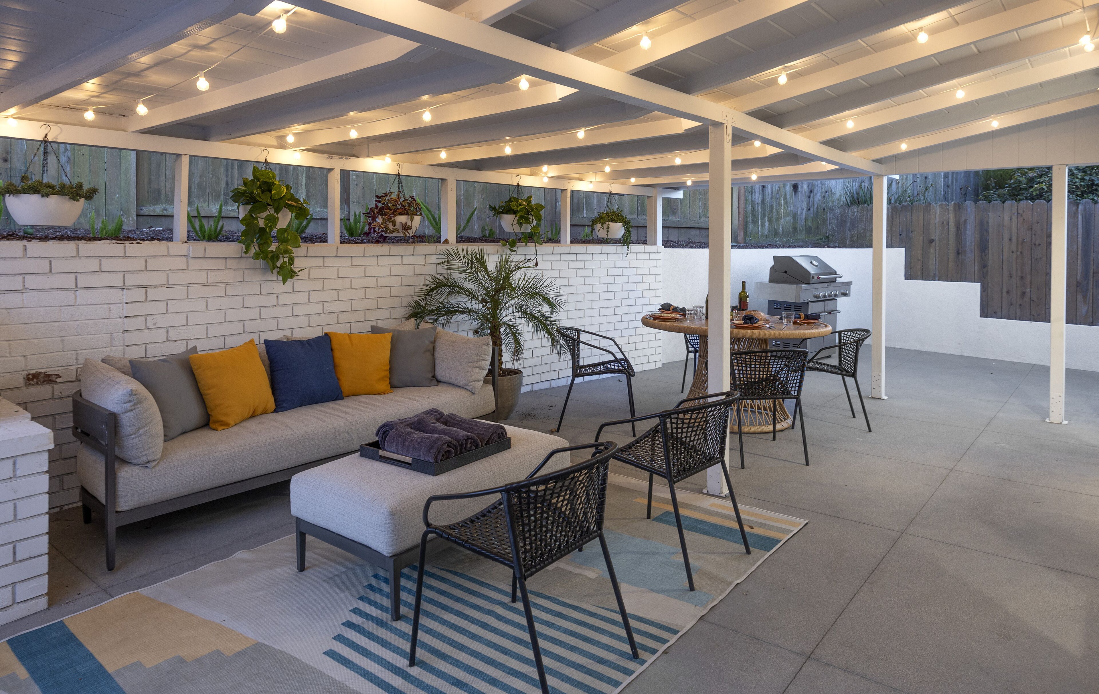 A covered outdoor seating area with a sofa, chairs, and a grill.
