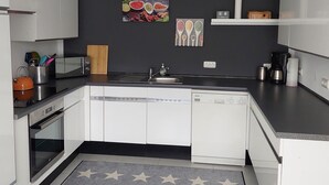 Eine moderne Küche mit weißen Schränken, einer schwarzen Arbeitsplatte, einem eingebauten Geschirrspüler und einem grauen Teppich mit Sternenmuster.