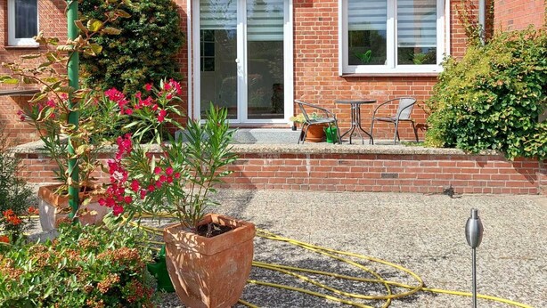 Ein zweigeschossiges Haus mit einem Ziegeldach, einer Ziegelverkleidung und einem kleinen Garten mit Blumentöpfen und Blumen.