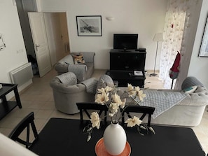 Un salon avec un canapé, un téléviseur, un meuble noir et un vase rempli de fleurs posé sur une table.