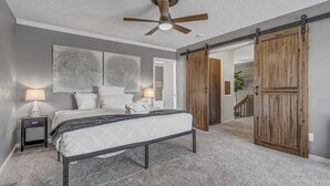 A bedroom with a bed, a ceiling fan, a nightstand, and a sliding barn-style door. - Inviting 5 Bedroom Home Centrally Located (Colorado Springs)
