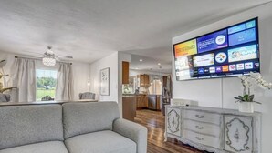 A living room with a grey sofa, a white cabinet, and a flat-screen TV mounted on the wall displaying various channels. - Inviting 5 Bedroom Home Centrally Located (Colorado Springs)