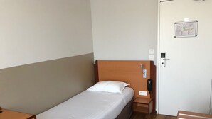Ein Einzelbett mit Holz Kopfteil, ein Nachttisch, ein Telefon und eine Tür mit einem Schild.