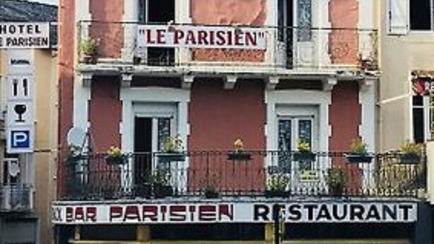 Ein Gebäude mit einem Schild, auf dem „LE PARISIEN“ und „BAR PARISIEN RESTAURANT“ steht, das ein Restaurant kennzeichnet.