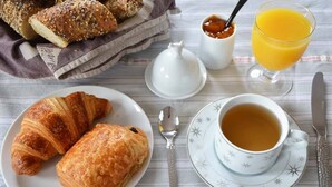 Ein Frühstückstisch mit Croissants, einer Teetasse und einem Glas Orangensaft.