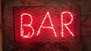 Ein Neon-Schild mit dem Wort "BAR" in Großbuchstaben, umrahmt von einem metallenen Rahmen mit Rautenmuster.