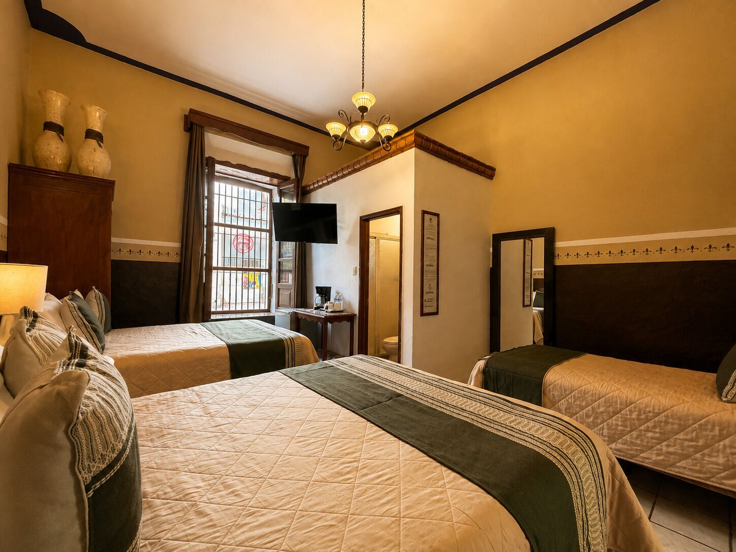 A hotel room with two beds, a television, a desk, and a window with barred glass.