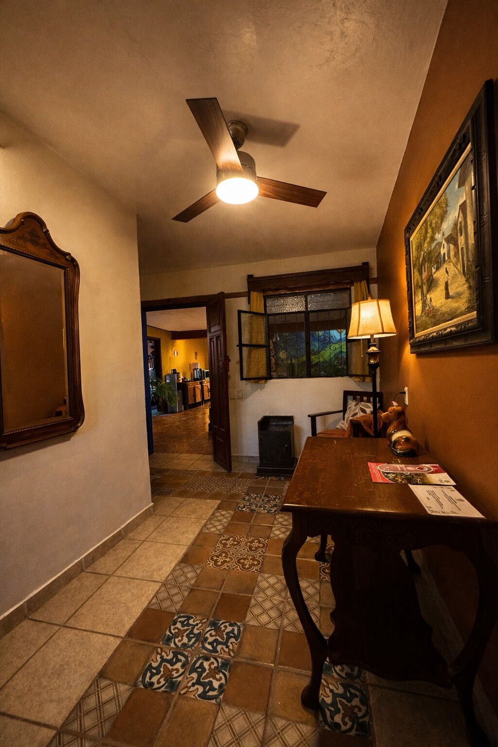 Une pièce dotée d’un ventilateur de plafond, d’une table à manger avec des chaises, d’un tableau encadré au mur et d’un sol à motifs.