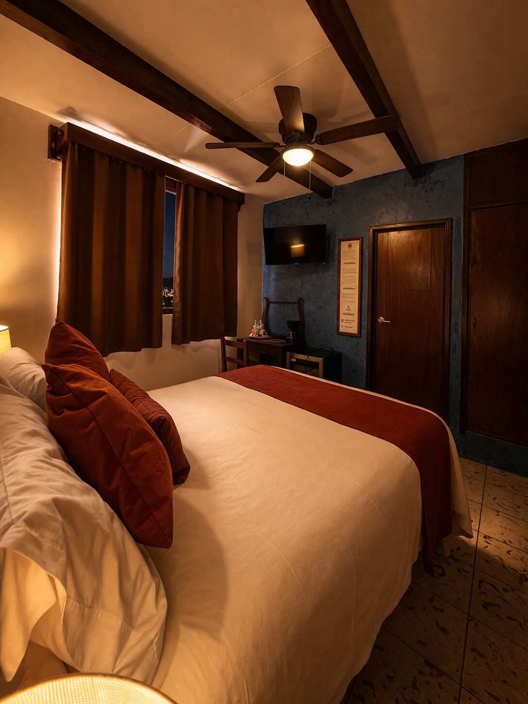 Une chambre d’hôtel avec un lit, un bureau, un ventilateur de plafond, une télévision et une porte.