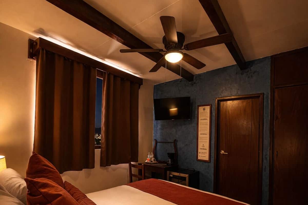 Une chambre d’hôtel avec un lit, un bureau, un ventilateur de plafond, une télévision et une porte.