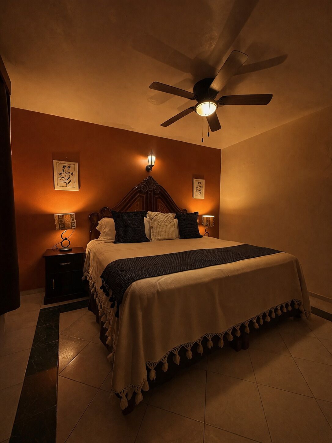 Une chambre à coucher comprenant un lit, un ventilateur de plafond, des lampes fixées au mur et une table de chevet.