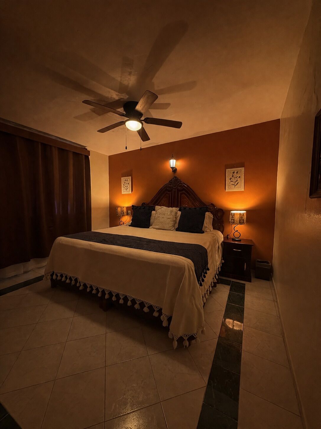 Une chambre à coucher comprenant un lit, un ventilateur de plafond, une table de chevet et des lampes fixées au mur.
