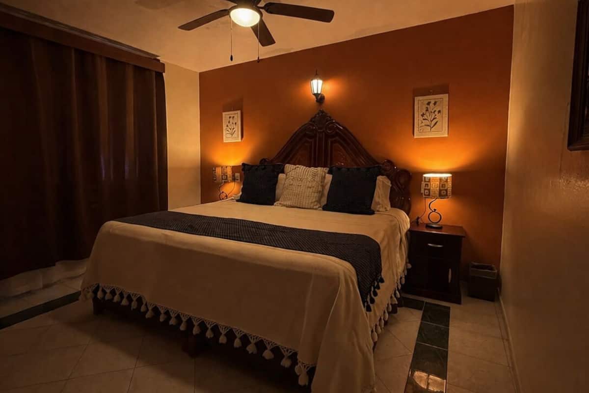 Une chambre à coucher comprenant un lit, un ventilateur de plafond, une table de chevet et des lampes fixées au mur.