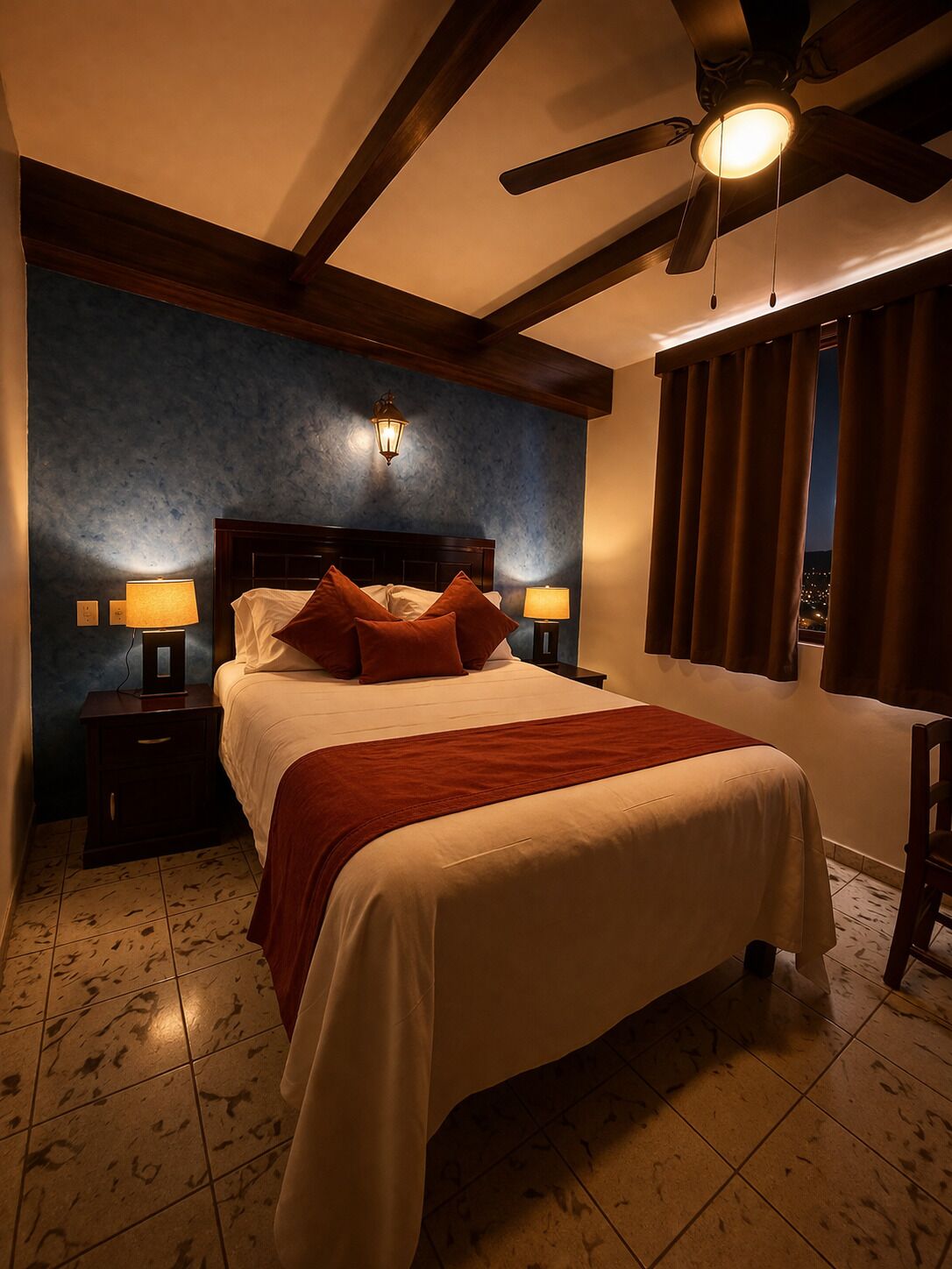 Ein Schlafzimmer mit einem Bett, zwei Nachttischen mit Lampen, einem Deckenventilator und Blick durch ein Fenster.