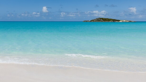 Una playa con aguas turquesas cristalinas y una pequeña isla a lo lejos.