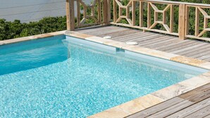 Una terraza de madera con piscina, rodeada de exuberante vegetación y vista al mar.