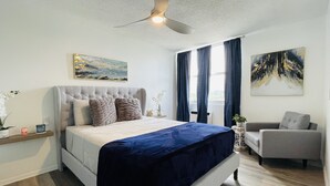 Ein Schlafzimmer mit einem Bett, einem Sessel, einem Deckenventilator und Bildern an den Wänden.