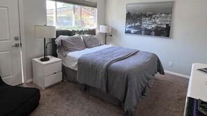 Ein Schlafzimmer mit einem Bett, zwei Nachttischen mit Lampen, einem Fenster mit Jalousien und einem Stadtbild an der Wand.