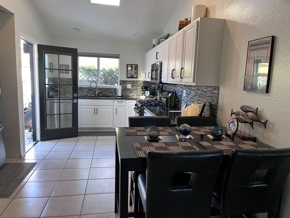 A modern kitchen with white cabinets, a black countertop, and a dining area with a black table and chairs. - Walk to the Beach and W Cliff Drive (Santa Cruz)