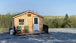 A small wooden cabin with a porch, two green chairs, and a door.