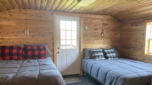 A cabin with two beds, each with a checkered blanket and pillows, a wooden ceiling, and a door with a window.