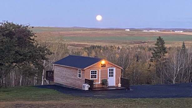 A wooden cabin with a porch, a small shed, and a clear view of the moon in the sky.