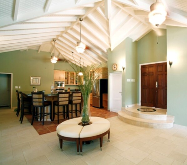 A spacious kitchen with a dining area, featuring a high ceiling with exposed beams, a central island, and a large wooden door. - Spacious 3 bedroom villa with pool in Red Pond (Sint Maarten)