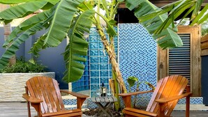 Eine Terrasse mit zwei Holzstühlen und einem kleinen Tisch, umgeben von einer gefliesten Wand und einer großen Pflanze.